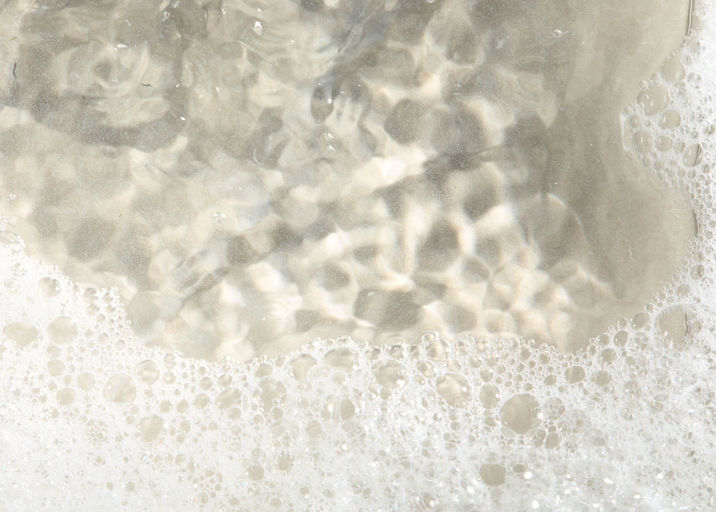 Close-up of water with bubbles and reflections on a sandy bottom